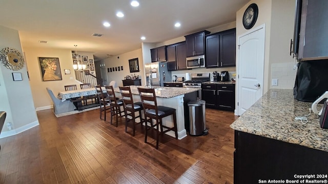 kitchen with a breakfast bar, appliances with stainless steel finishes, dark hardwood / wood-style floors, light stone counters, and decorative backsplash