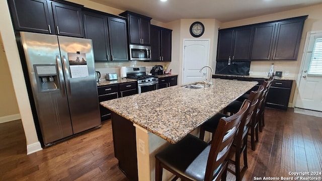 kitchen featuring sink, a center island with sink, appliances with stainless steel finishes, a kitchen breakfast bar, and light stone countertops