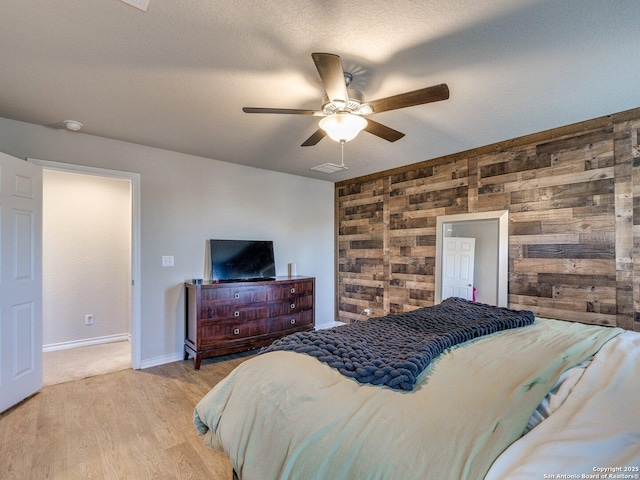 bedroom with ceiling fan, wooden walls, a textured ceiling, and light wood-type flooring