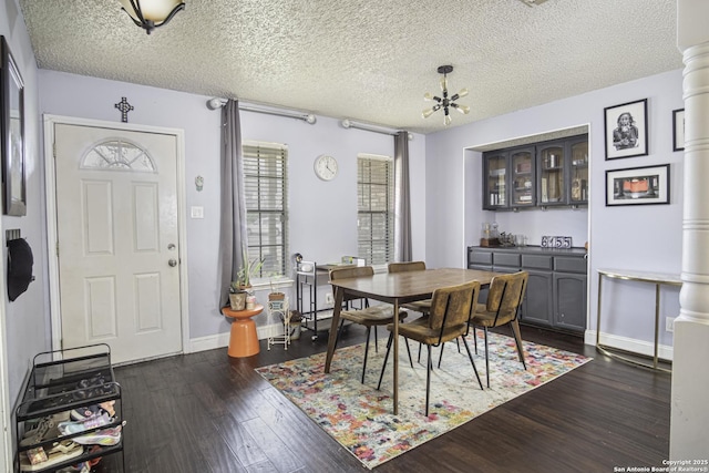 dining area with a notable chandelier, dark hardwood / wood-style flooring, a textured ceiling, and ornate columns