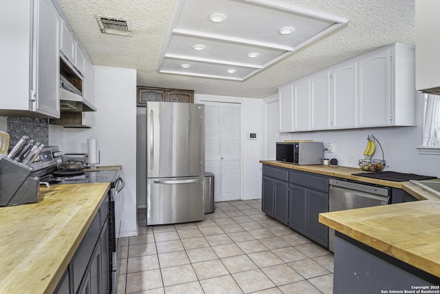 kitchen with light tile patterned flooring, appliances with stainless steel finishes, wood counters, white cabinetry, and a textured ceiling