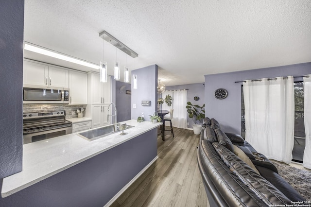 kitchen with sink, white cabinetry, wood-type flooring, hanging light fixtures, and appliances with stainless steel finishes