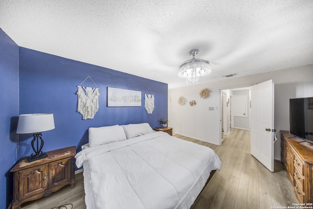 bedroom with wood-type flooring, an inviting chandelier, and a textured ceiling