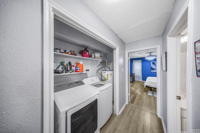 clothes washing area featuring water heater, washing machine and dryer, a textured ceiling, and light wood-type flooring