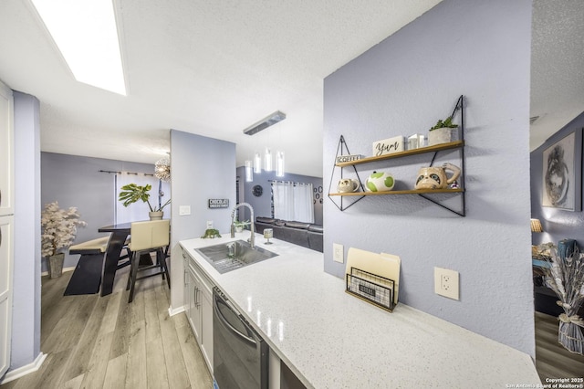 kitchen with decorative light fixtures, black dishwasher, sink, light stone counters, and light wood-type flooring