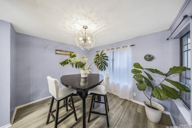 dining area with wood-type flooring, an inviting chandelier, and a textured ceiling