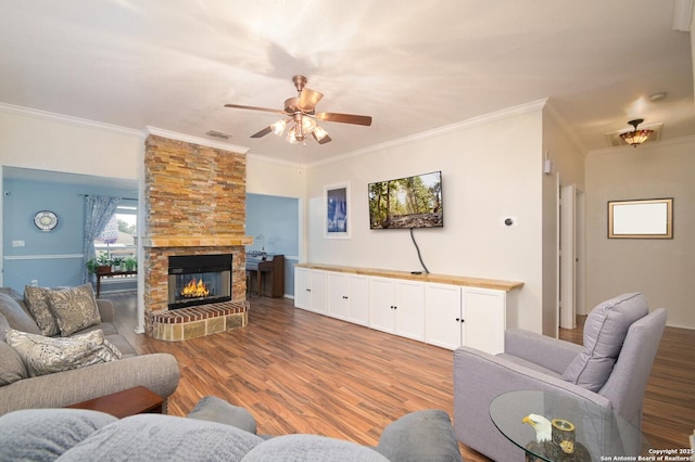 living room featuring a stone fireplace, wood-type flooring, ornamental molding, and ceiling fan