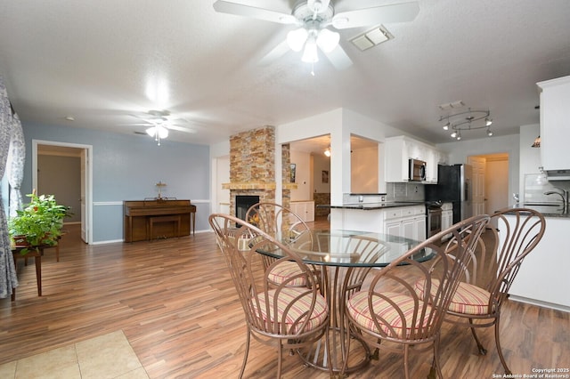 dining room with ceiling fan, a stone fireplace, light hardwood / wood-style floors, and a textured ceiling