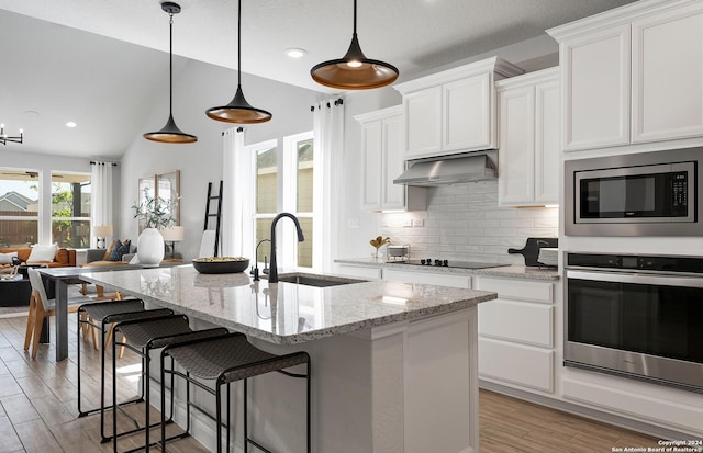 kitchen with sink, white cabinetry, an island with sink, stainless steel appliances, and light stone countertops