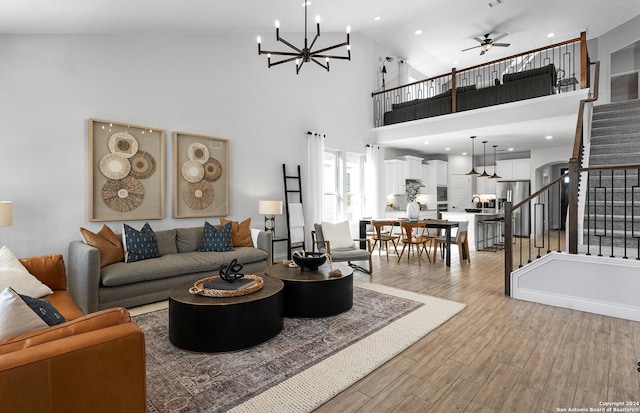 living room with sink, ceiling fan with notable chandelier, light hardwood / wood-style flooring, and a high ceiling