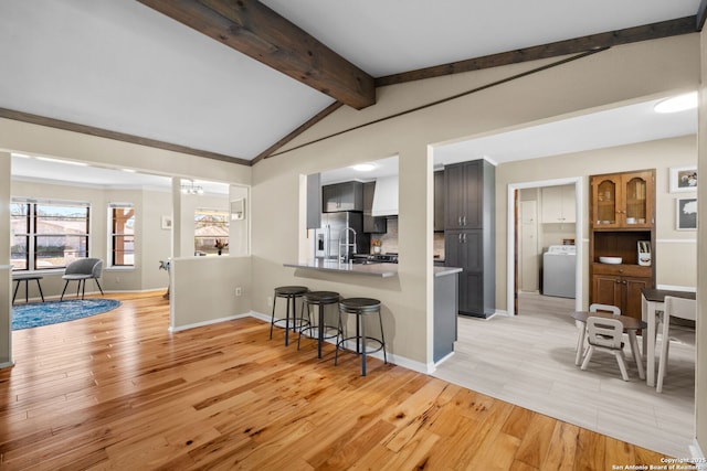 kitchen with a breakfast bar, vaulted ceiling with beams, light hardwood / wood-style flooring, kitchen peninsula, and washer / clothes dryer