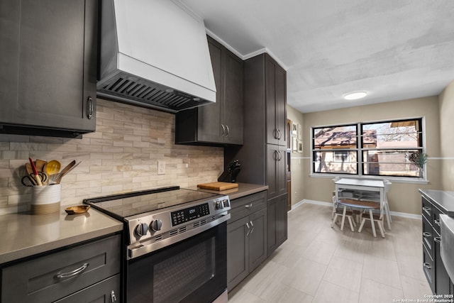 kitchen featuring dark brown cabinets, decorative backsplash, wall chimney exhaust hood, and stainless steel range with electric cooktop