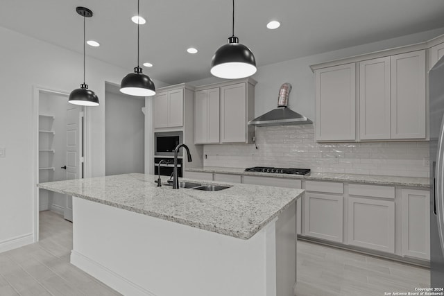 kitchen featuring hanging light fixtures, a kitchen island with sink, sink, and light stone countertops