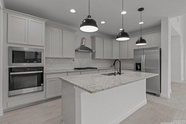 kitchen featuring stainless steel appliances, sink, wall chimney range hood, and a kitchen island with sink