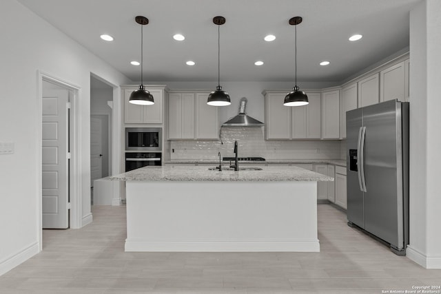 kitchen with an island with sink, sink, stainless steel fridge, light stone countertops, and wall chimney exhaust hood