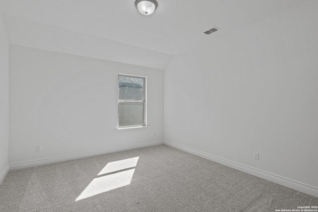 carpeted empty room with vaulted ceiling