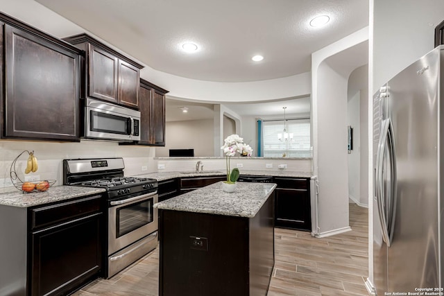 kitchen with pendant lighting, sink, appliances with stainless steel finishes, a kitchen island, and kitchen peninsula