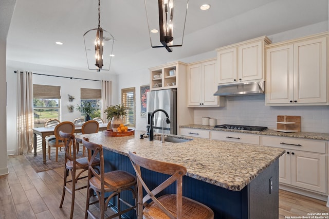 kitchen featuring sink, stainless steel fridge, hanging light fixtures, an island with sink, and decorative backsplash