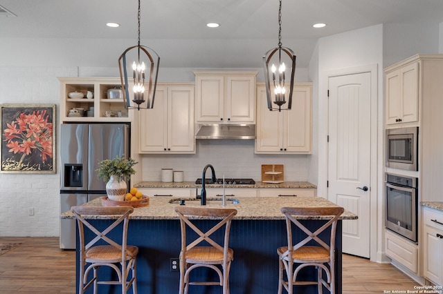 kitchen with hanging light fixtures, appliances with stainless steel finishes, a kitchen island with sink, and light stone counters