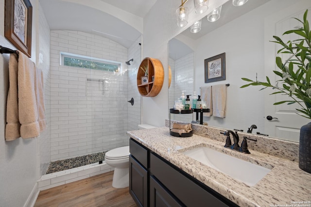 bathroom featuring hardwood / wood-style flooring, vanity, a tile shower, and toilet