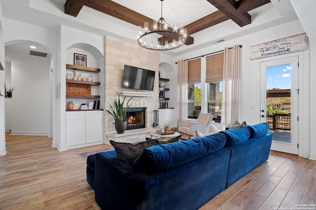 living room featuring coffered ceiling, a stone fireplace, a chandelier, light hardwood / wood-style flooring, and beamed ceiling