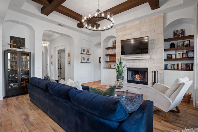 living room featuring beamed ceiling, a stone fireplace, built in features, and light wood-type flooring