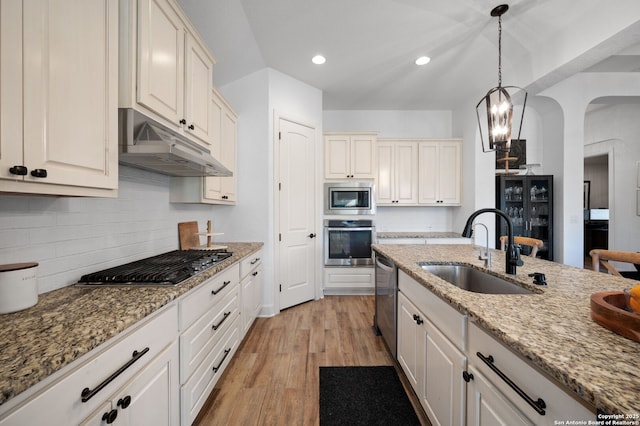 kitchen with sink, appliances with stainless steel finishes, pendant lighting, light stone countertops, and light hardwood / wood-style floors