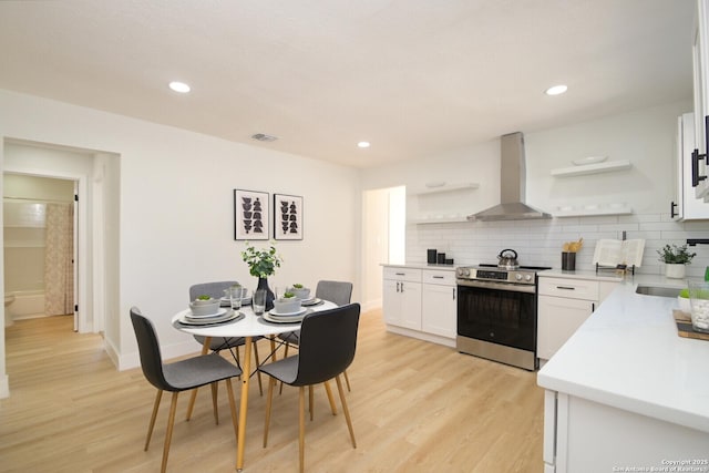 kitchen featuring wall chimney range hood, stainless steel electric range, light hardwood / wood-style flooring, white cabinets, and decorative backsplash