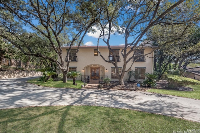 mediterranean / spanish home with a front lawn, french doors, and a balcony