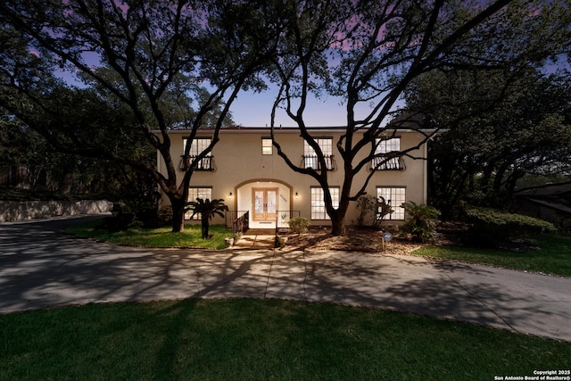 view of front of house with french doors, a balcony, and a lawn