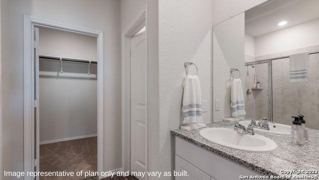 bathroom featuring a shower stall, a walk in closet, and vanity