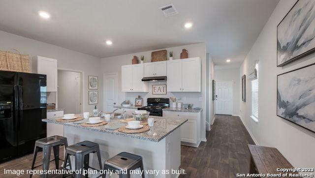 kitchen featuring dark wood finished floors, a kitchen bar, under cabinet range hood, visible vents, and black appliances