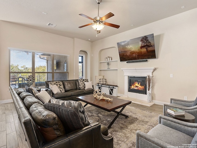 living room featuring built in shelves, ceiling fan, and light hardwood / wood-style flooring