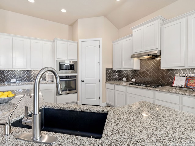 kitchen with lofted ceiling, sink, stainless steel appliances, light stone countertops, and white cabinets