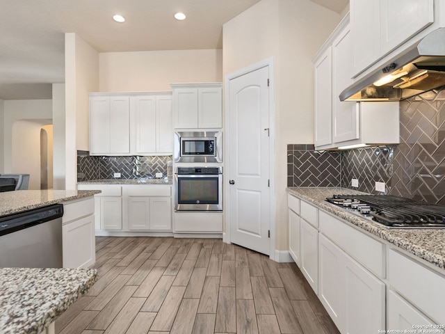 kitchen with appliances with stainless steel finishes, tasteful backsplash, white cabinetry, light stone counters, and light hardwood / wood-style floors