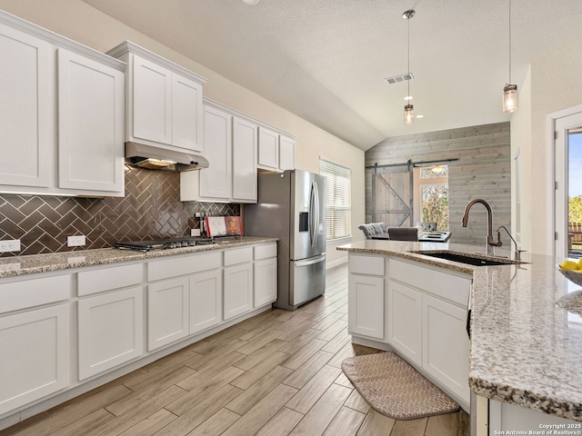 kitchen with appliances with stainless steel finishes, sink, white cabinets, hanging light fixtures, and a barn door