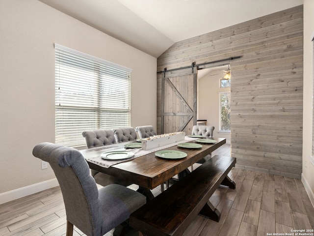 dining area with vaulted ceiling, a barn door, wooden walls, and light hardwood / wood-style floors