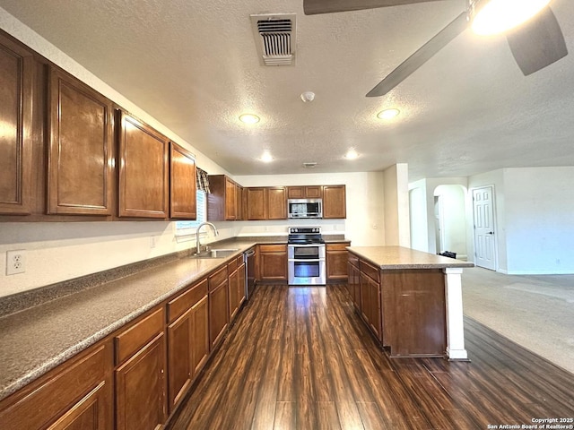 kitchen with sink, appliances with stainless steel finishes, a center island, dark hardwood / wood-style floors, and a textured ceiling