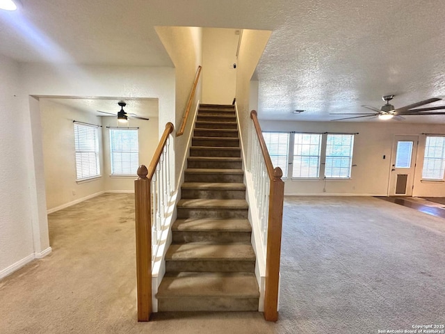 staircase featuring ceiling fan, plenty of natural light, carpet floors, and a textured ceiling