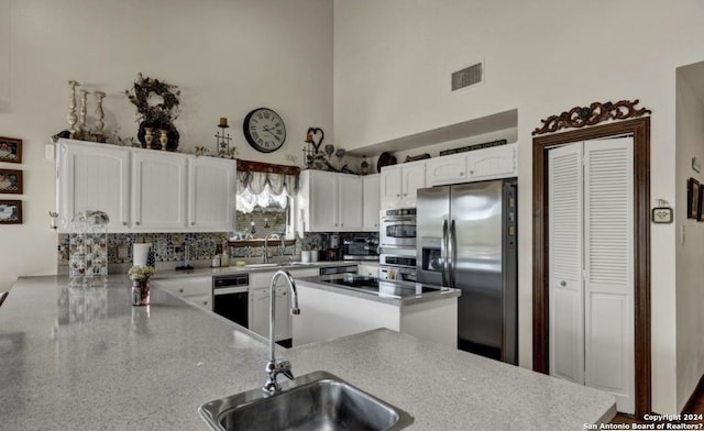 kitchen featuring sink, appliances with stainless steel finishes, a high ceiling, white cabinets, and kitchen peninsula