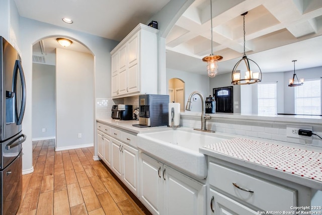 kitchen with stainless steel refrigerator with ice dispenser, tasteful backsplash, decorative light fixtures, light wood-type flooring, and white cabinets