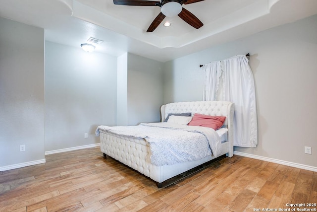 bedroom with light hardwood / wood-style floors, a raised ceiling, and ceiling fan