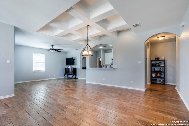 unfurnished living room with beam ceiling, coffered ceiling, ceiling fan with notable chandelier, and light hardwood / wood-style floors