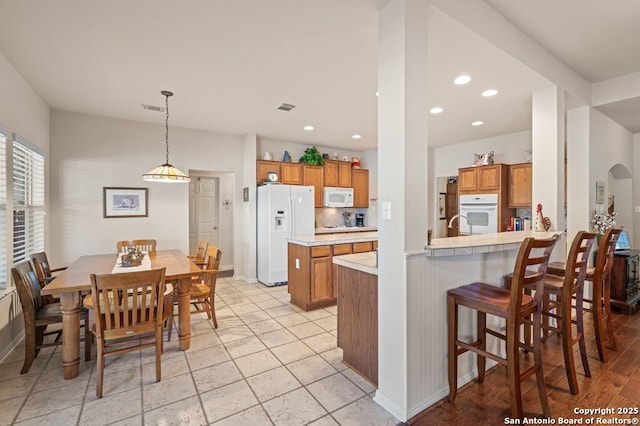 kitchen featuring hanging light fixtures, tasteful backsplash, white appliances, and kitchen peninsula