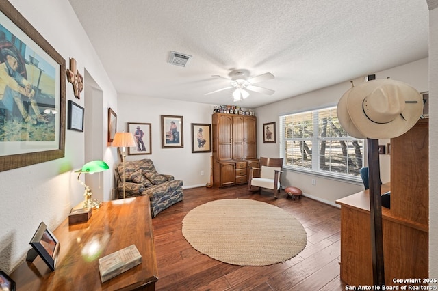 living area with dark wood-type flooring, ceiling fan, and a textured ceiling