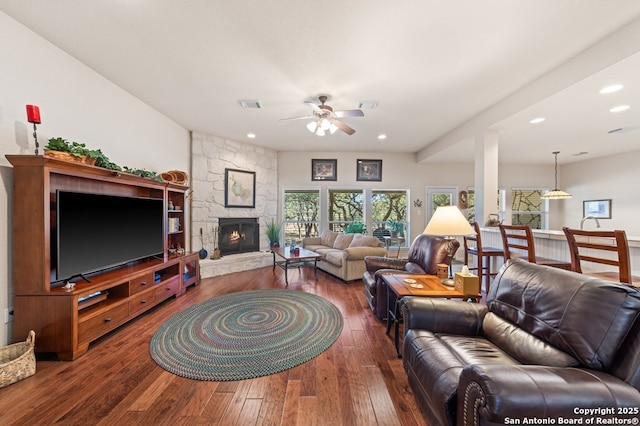 living room with dark wood-type flooring, ceiling fan, and a stone fireplace