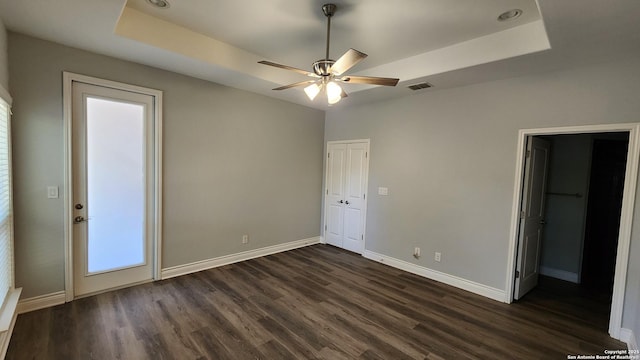 unfurnished bedroom with a tray ceiling, dark wood-type flooring, ensuite bath, and ceiling fan