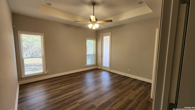 unfurnished room featuring dark wood-type flooring, a healthy amount of sunlight, and a tray ceiling