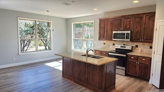 kitchen with sink, stainless steel appliances, light stone counters, a center island with sink, and decorative light fixtures