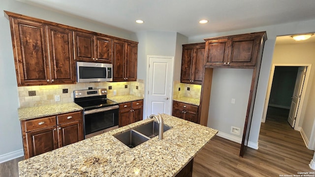 kitchen with sink, dark wood-type flooring, stainless steel appliances, light stone counters, and a center island with sink